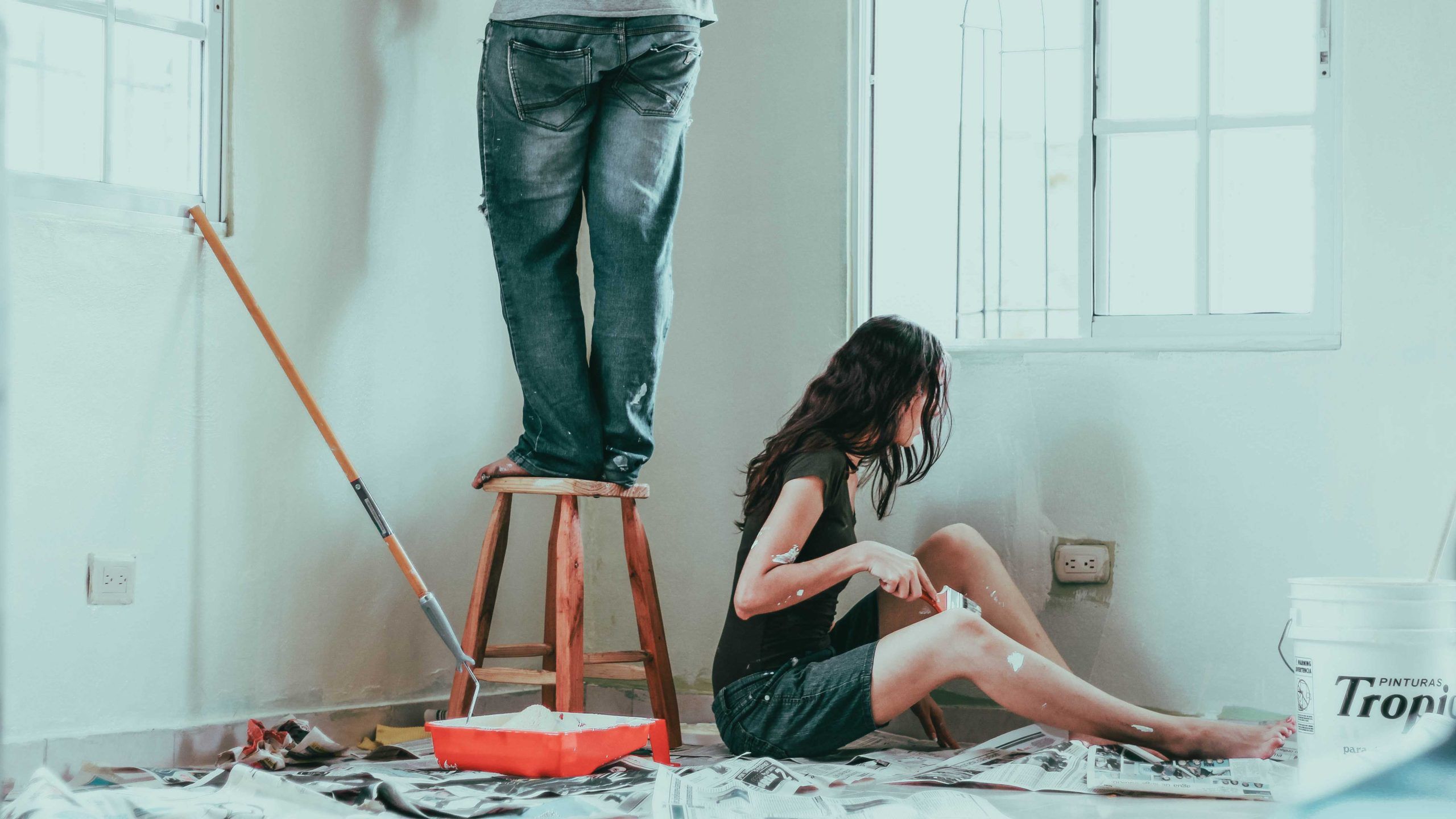 Two people attempting a home renovation - one person is on a stool and the other is sitting on the floor.